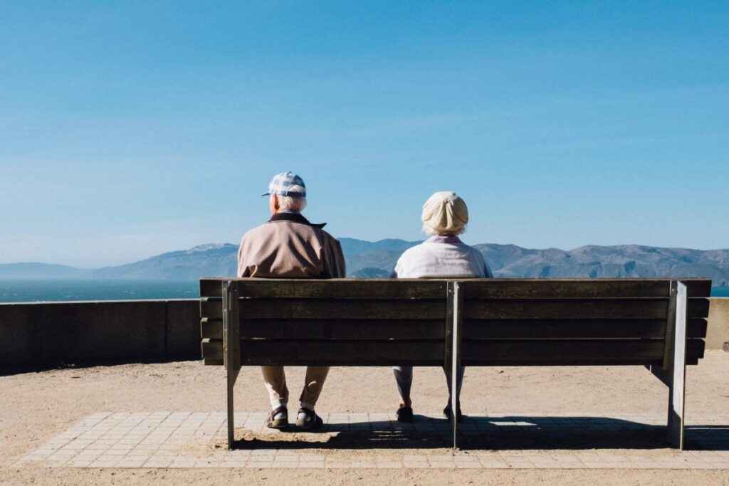 Et ældre par sidder på en bænk og kigger udover horisonten.
